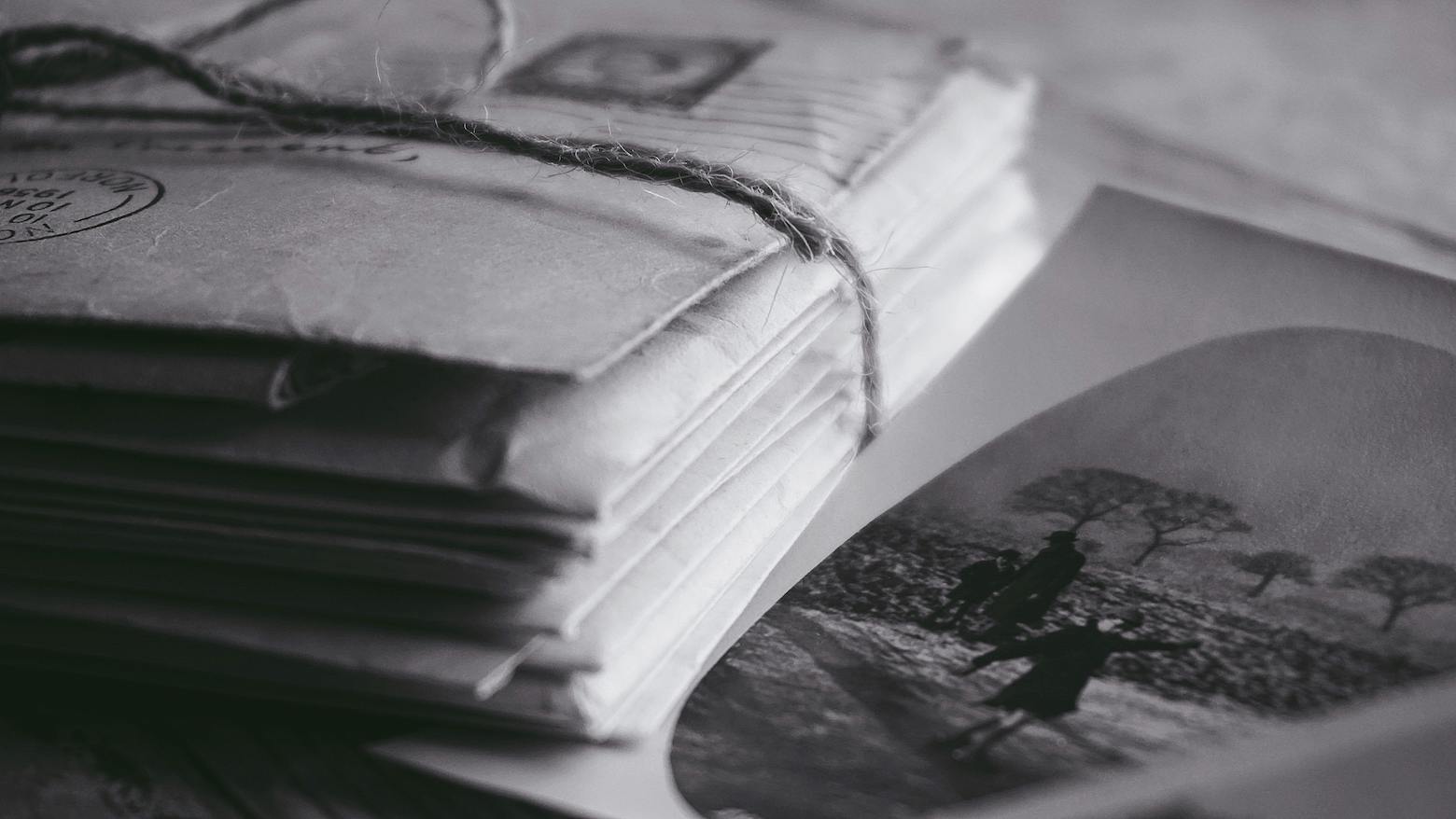 A black and white image showcasing a stack of vintage envelopes tied with string, highlighting their worn textures and nostalgic charm