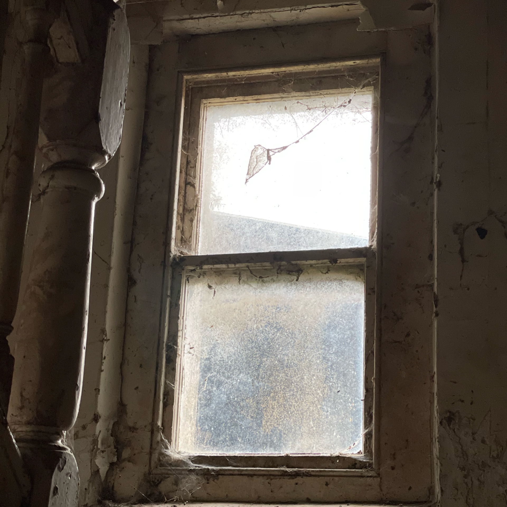 Weathered sash window with peeling paint and cracked glass in an old farmhouse.
