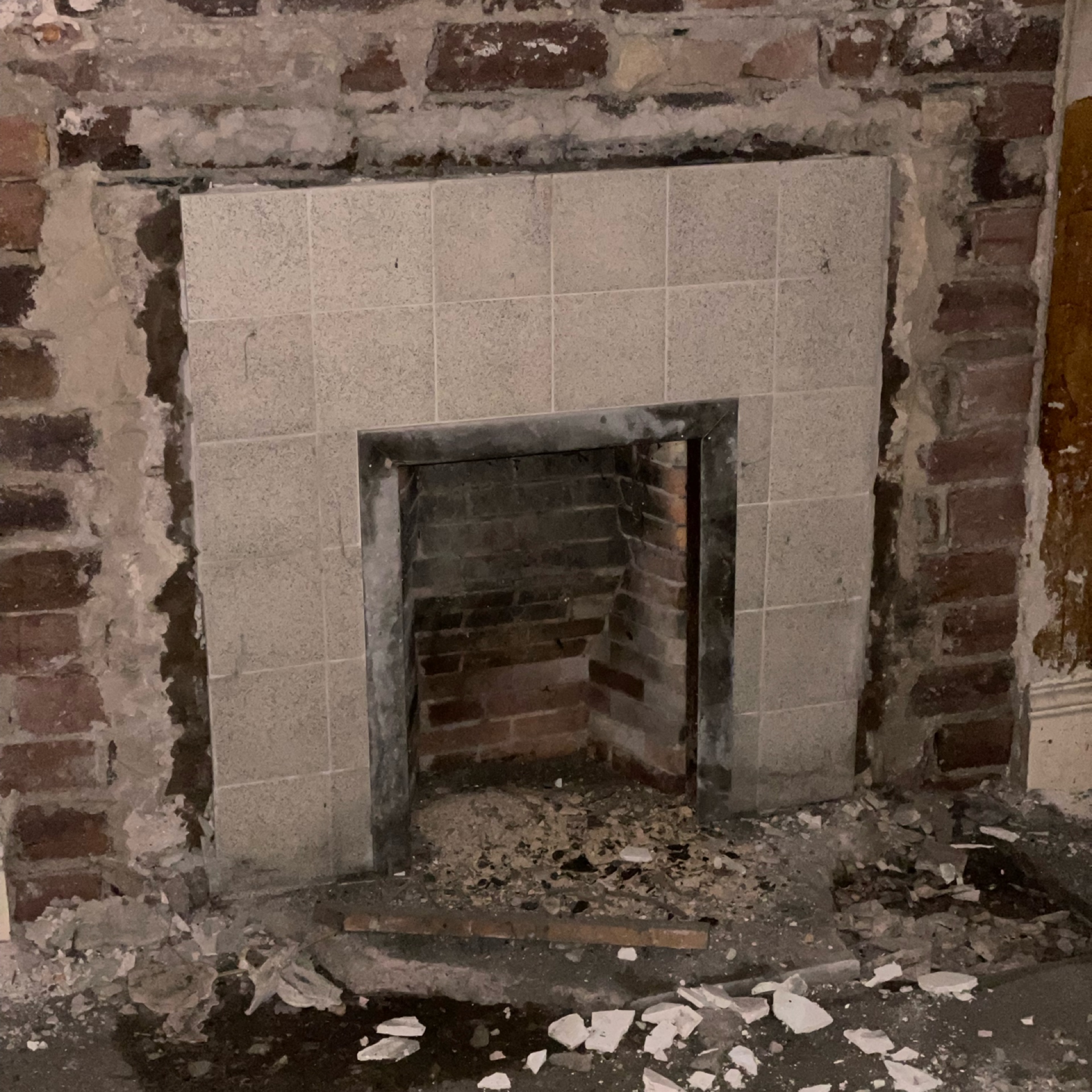 Exposed brick fireplace with modern granite surround in process of demolition.