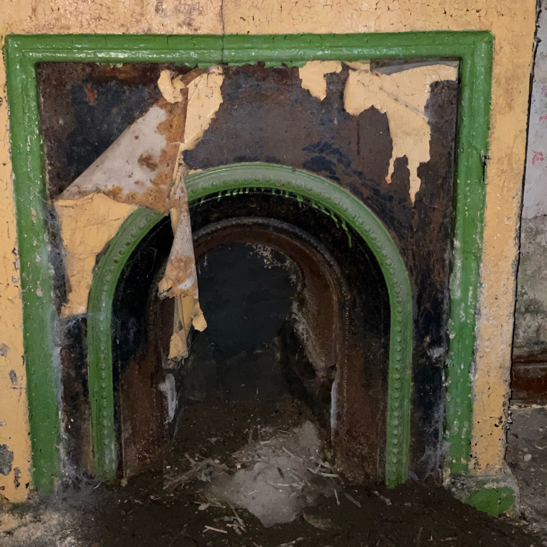 Vintage fireplace with green cast iron insert in deteriorating yellow painted wall.