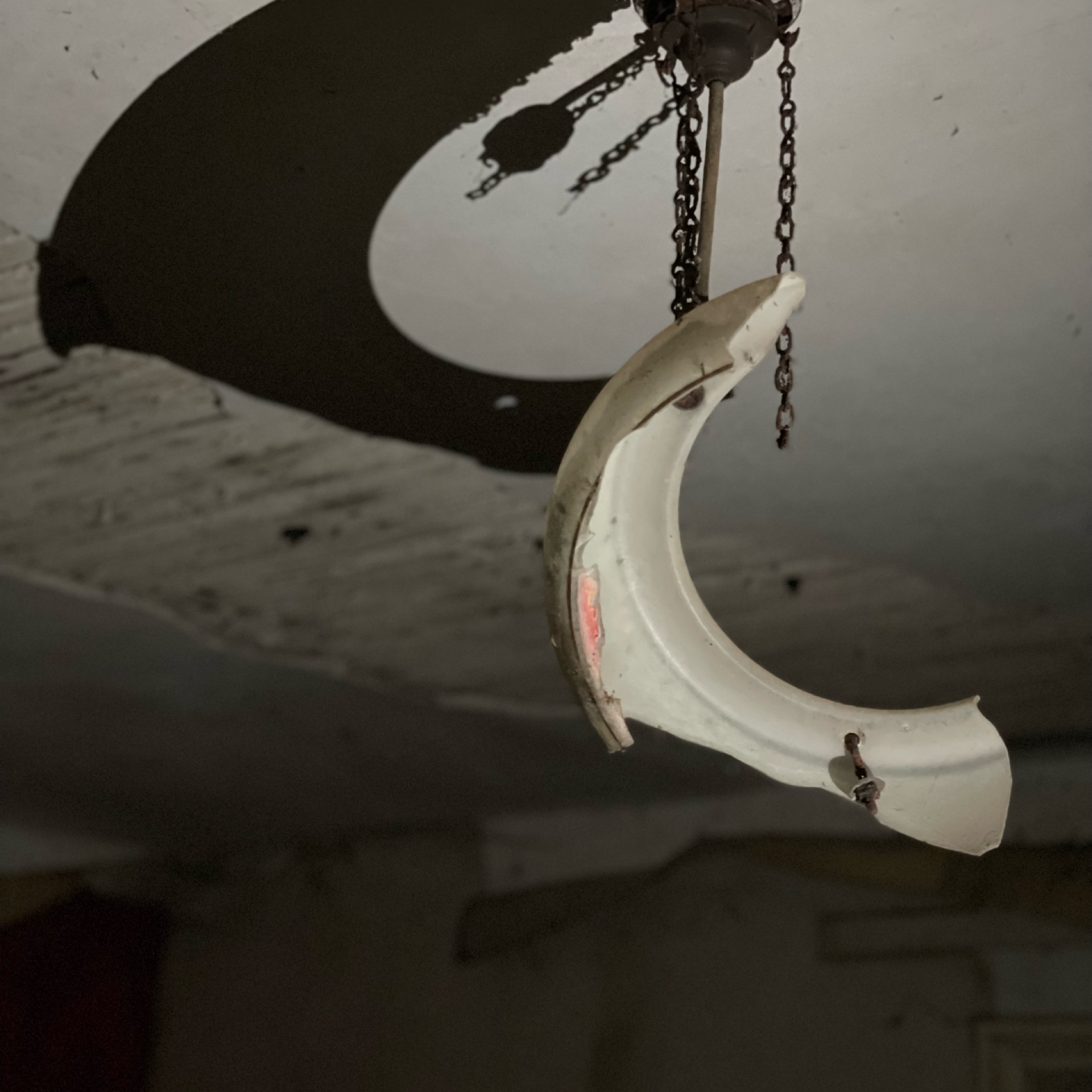 Broken porcelain light fixture hanging from ceiling in abandoned room.