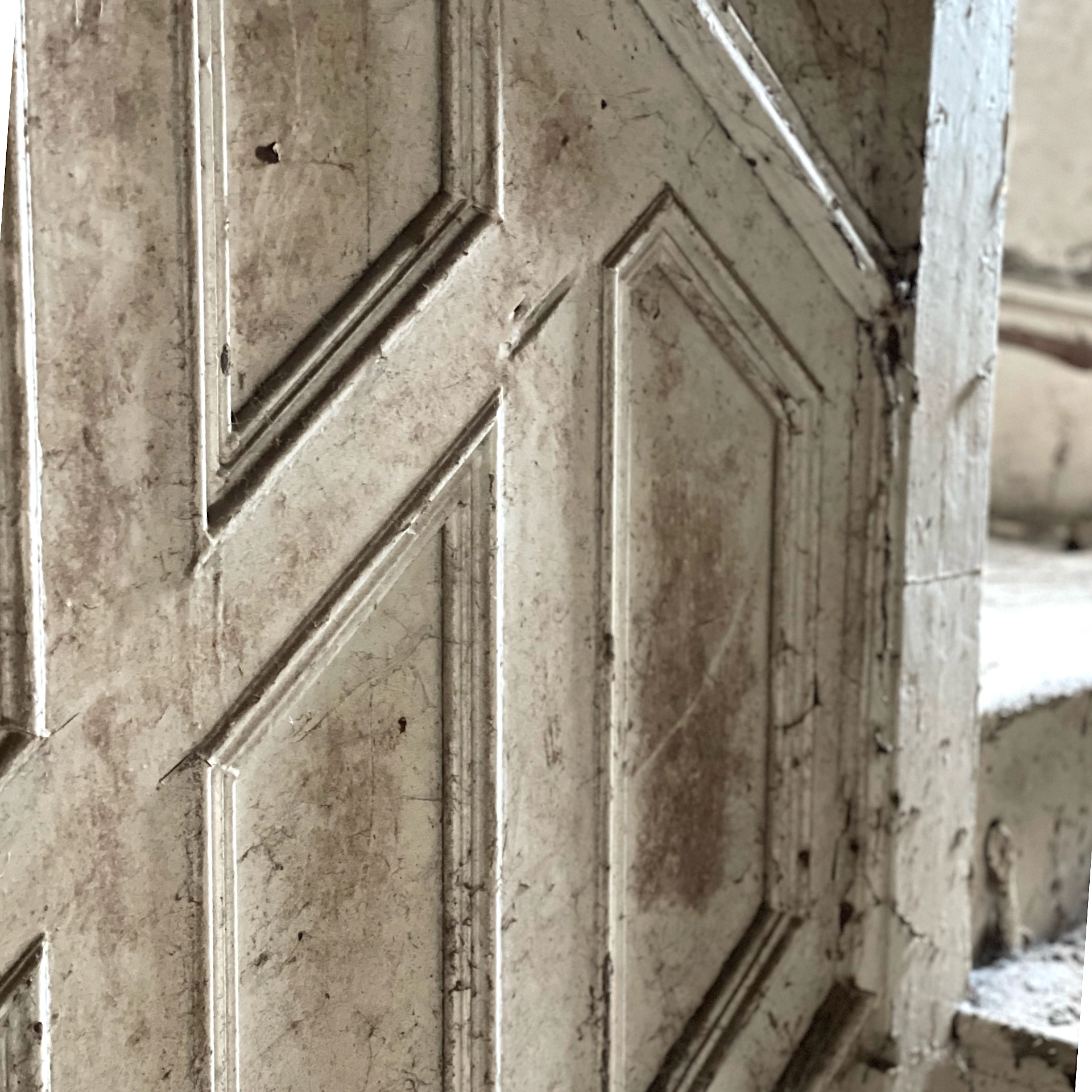 Close-up of a weathered, ornate stair panel with geometric patterns. The surface shows signs of aging, giving a vintage and textured feel.