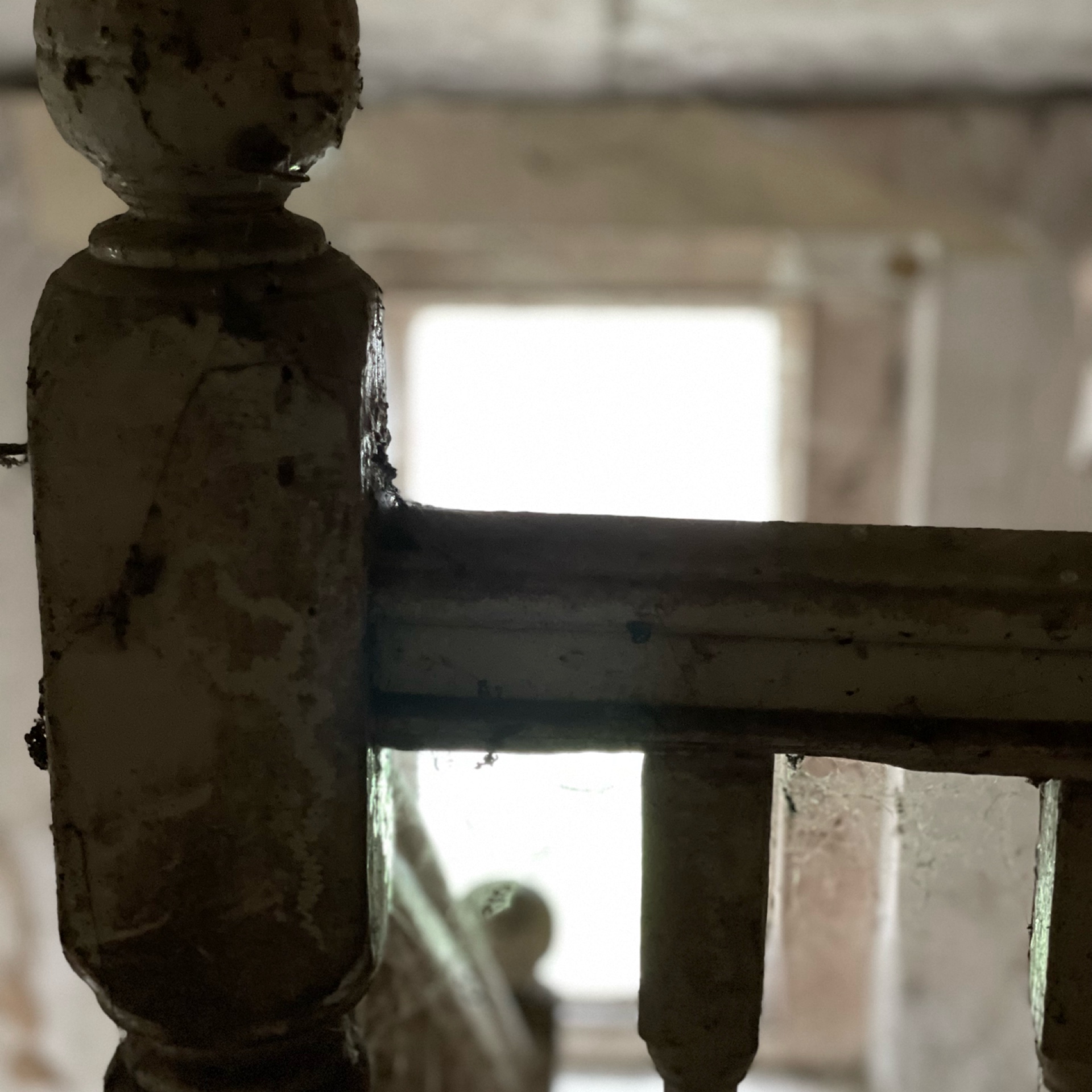 Detail of dilapidated staircase in an abandoned building. Peeling paint and cobwebs enhance the eerie and neglected atmosphere. A sash window provides light.