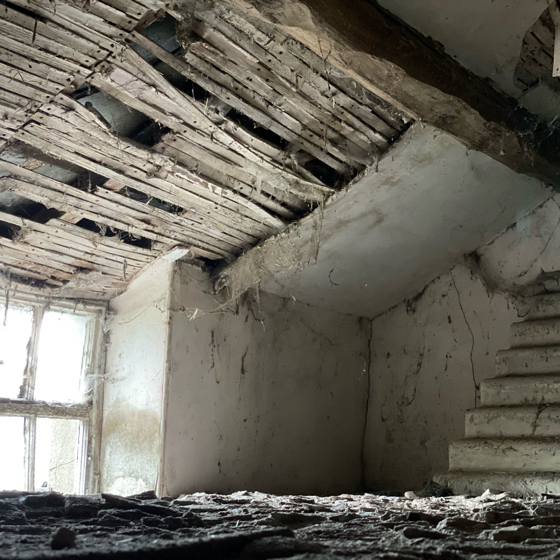 Exposed ceiling laths and damaged plaster in abandoned room with window.