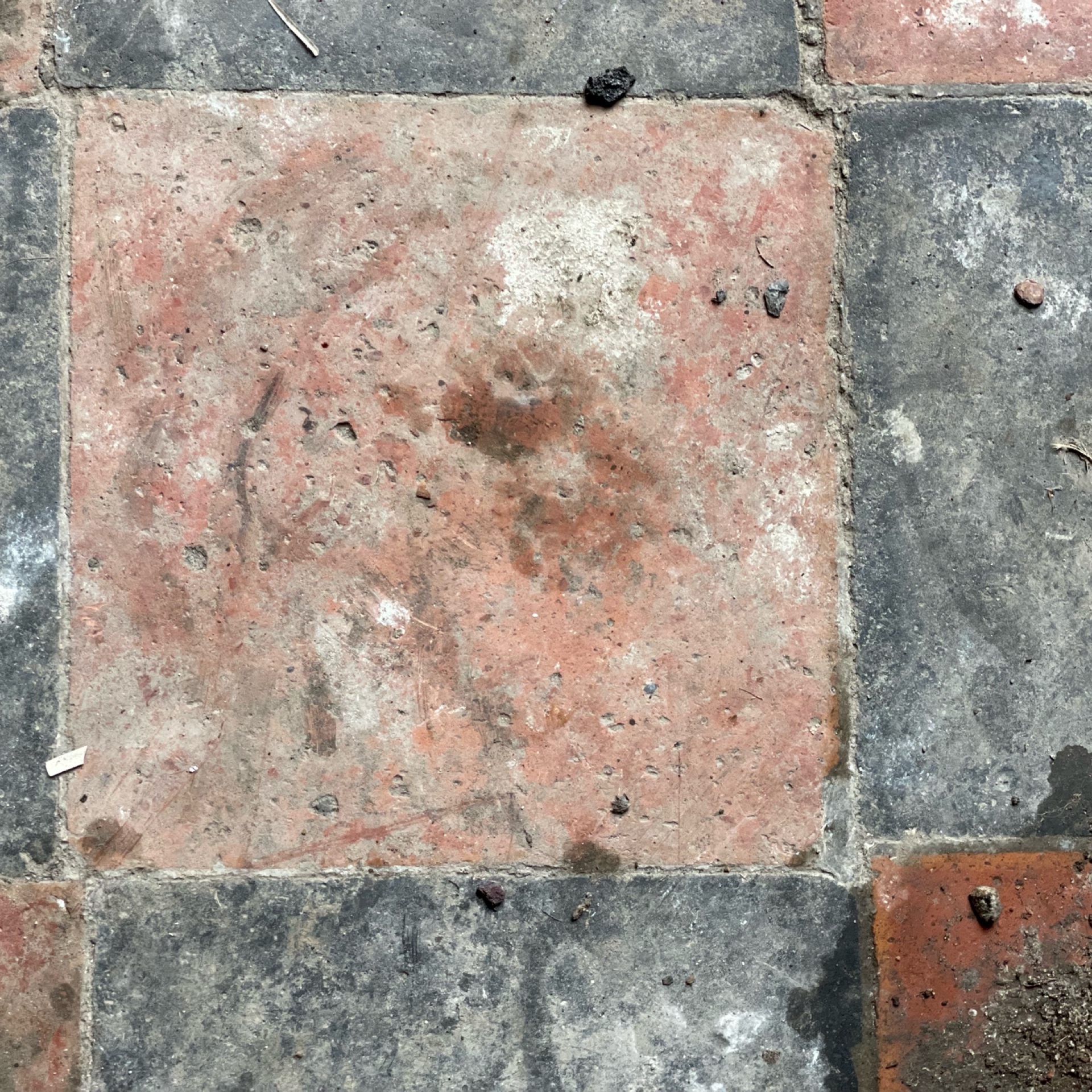 Weathered red and gray stone tiles with visible scuffs and dirt specks create a rustic, aged look. The tones suggest a historic setting.